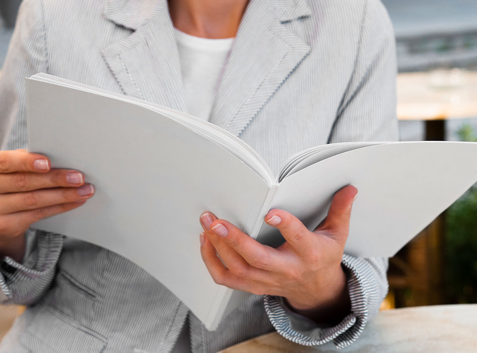 Un primer plano de una mujer con una chaqueta gris leyendo un libro abierto titulado "Quién Soy", con solo sus manos y el libro visibles.