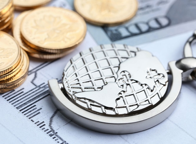 Un llavero de metal con un mapa del mundo apoyado sobre documentos financieros junto a pilas de monedas y papel moneda, que ilustra las tendencias de consumo global.